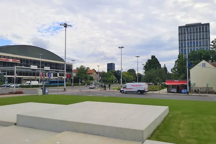 The arched roof of Zagreb's Dom sportova arena across a wide junction, with a Tisak kiosk and the Cibona tower behind